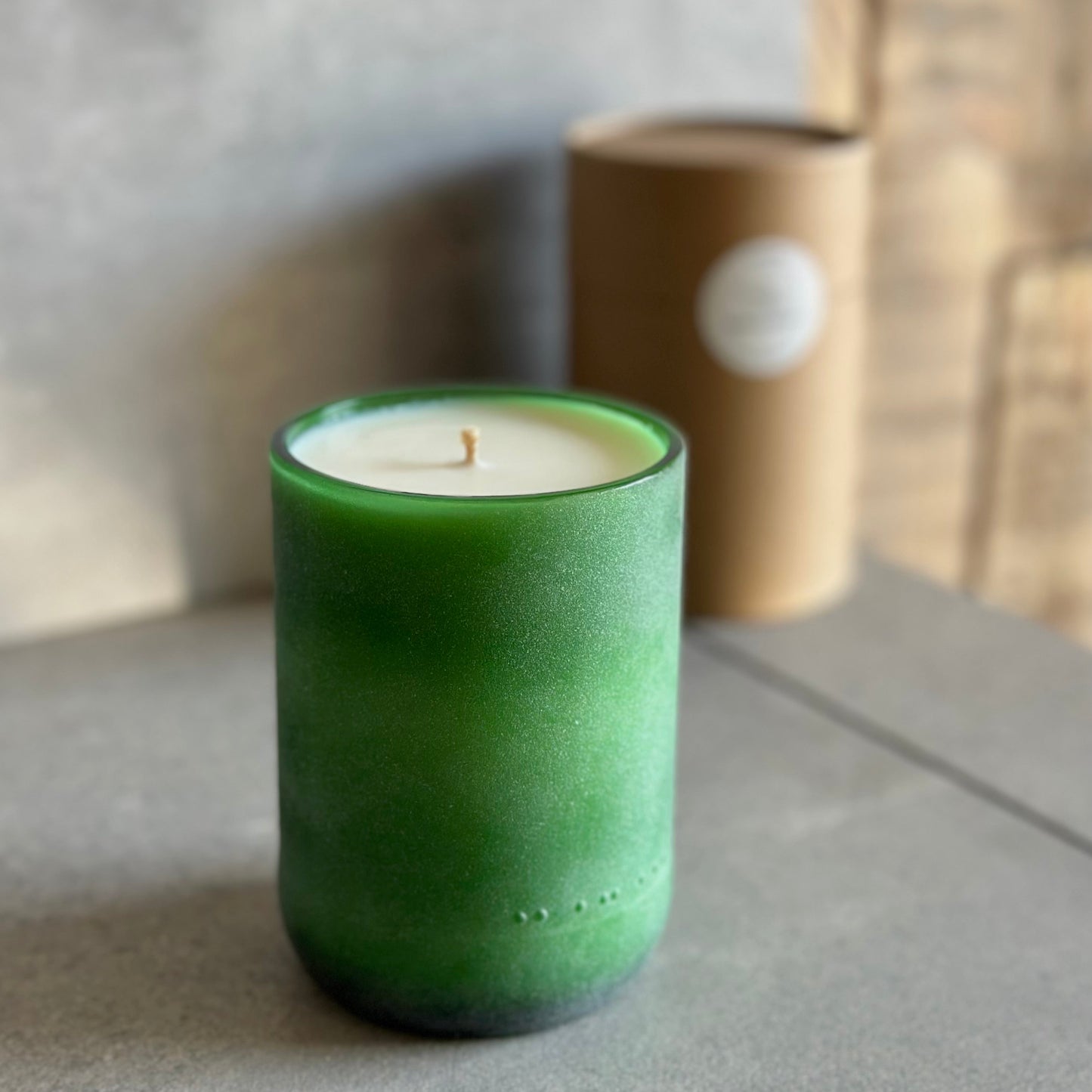 Green candle in a textured container on a gray surface with a blurred background
